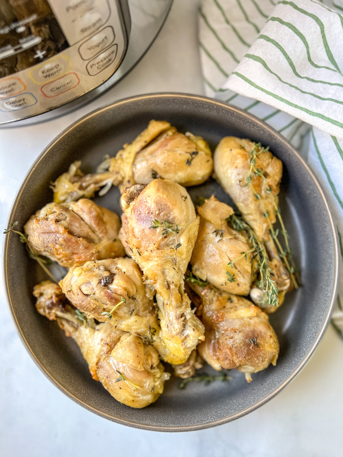 chicken drum sticks in a gray dish with thyme in front of an Instant Pot