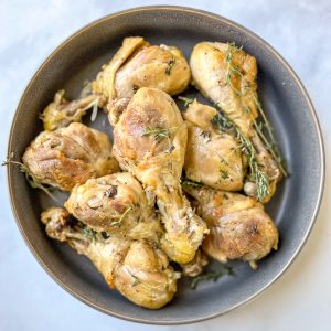 Coooked chicken drumsticks with thyme in a serving bowl