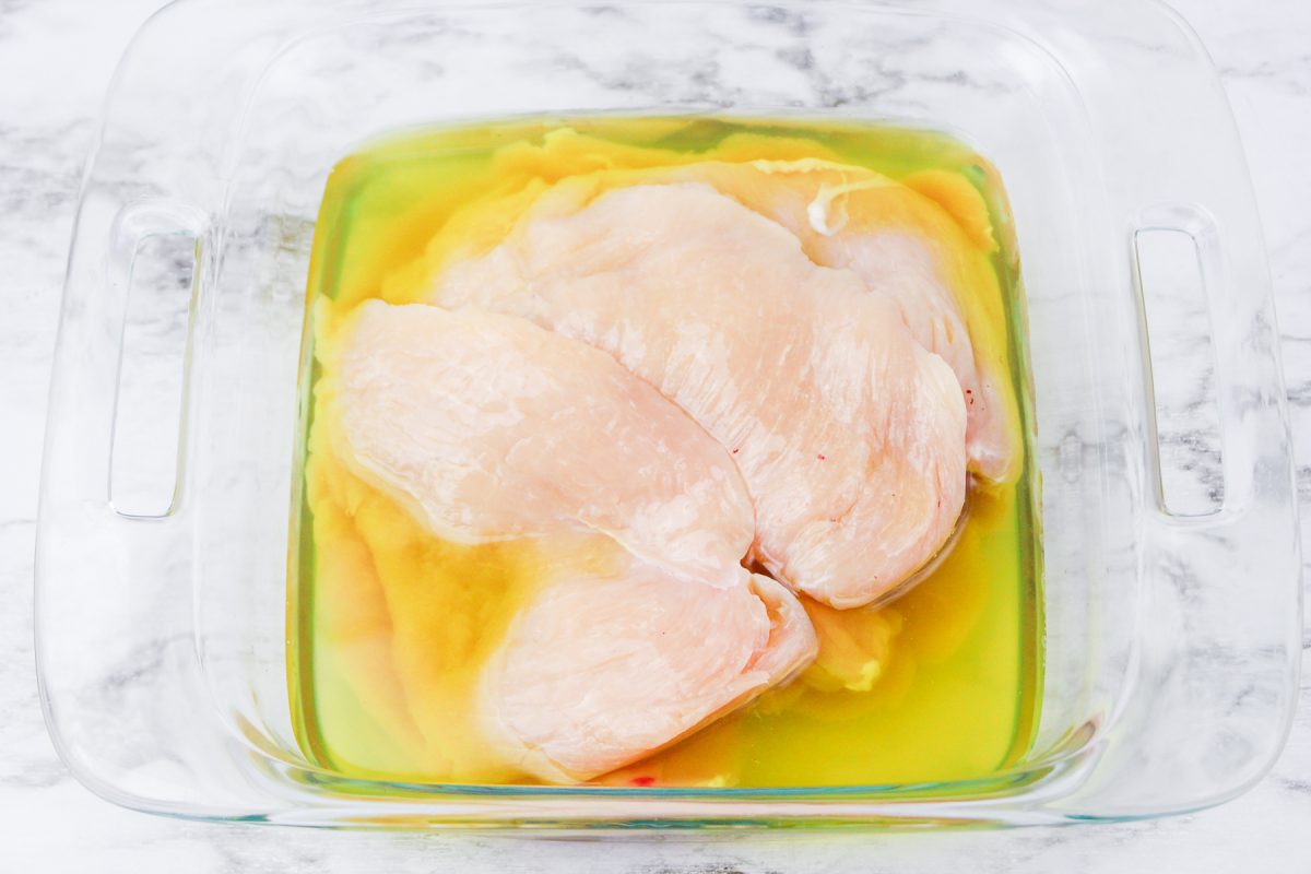 Marinating chicken breast in pickle juice in a glass container from overhead