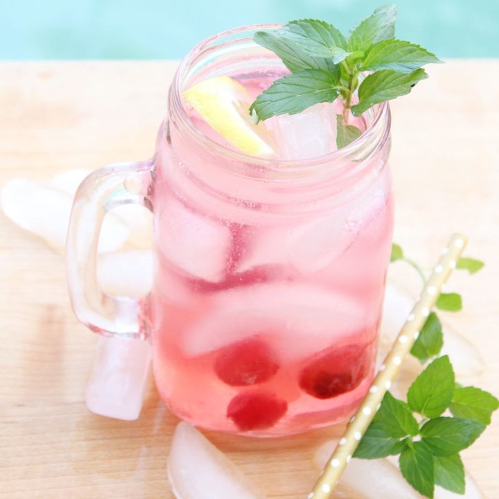A mason jar full of cherry lemonade and ice topped with a slice of lemon and a sprig of mint
