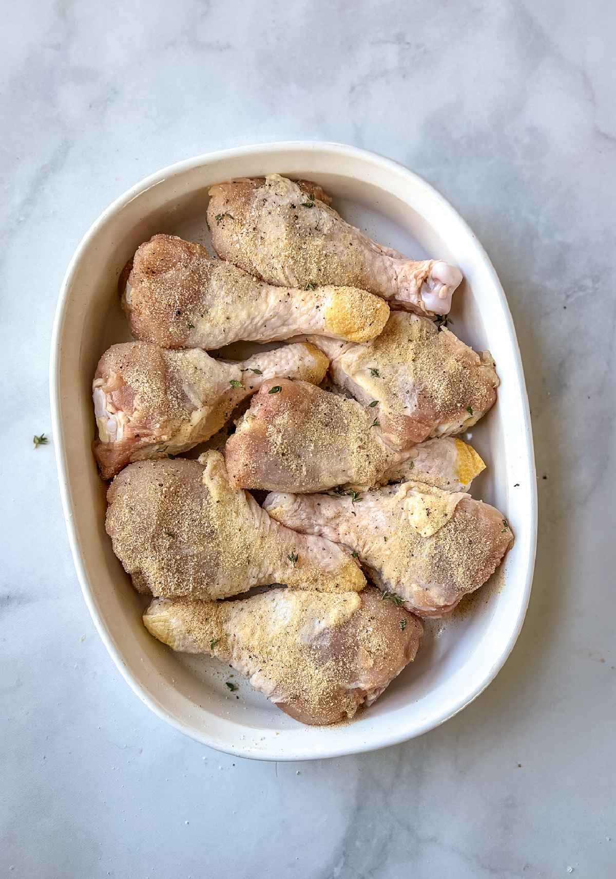 Uncooked and seasoned chicken drumsticks in a white dish