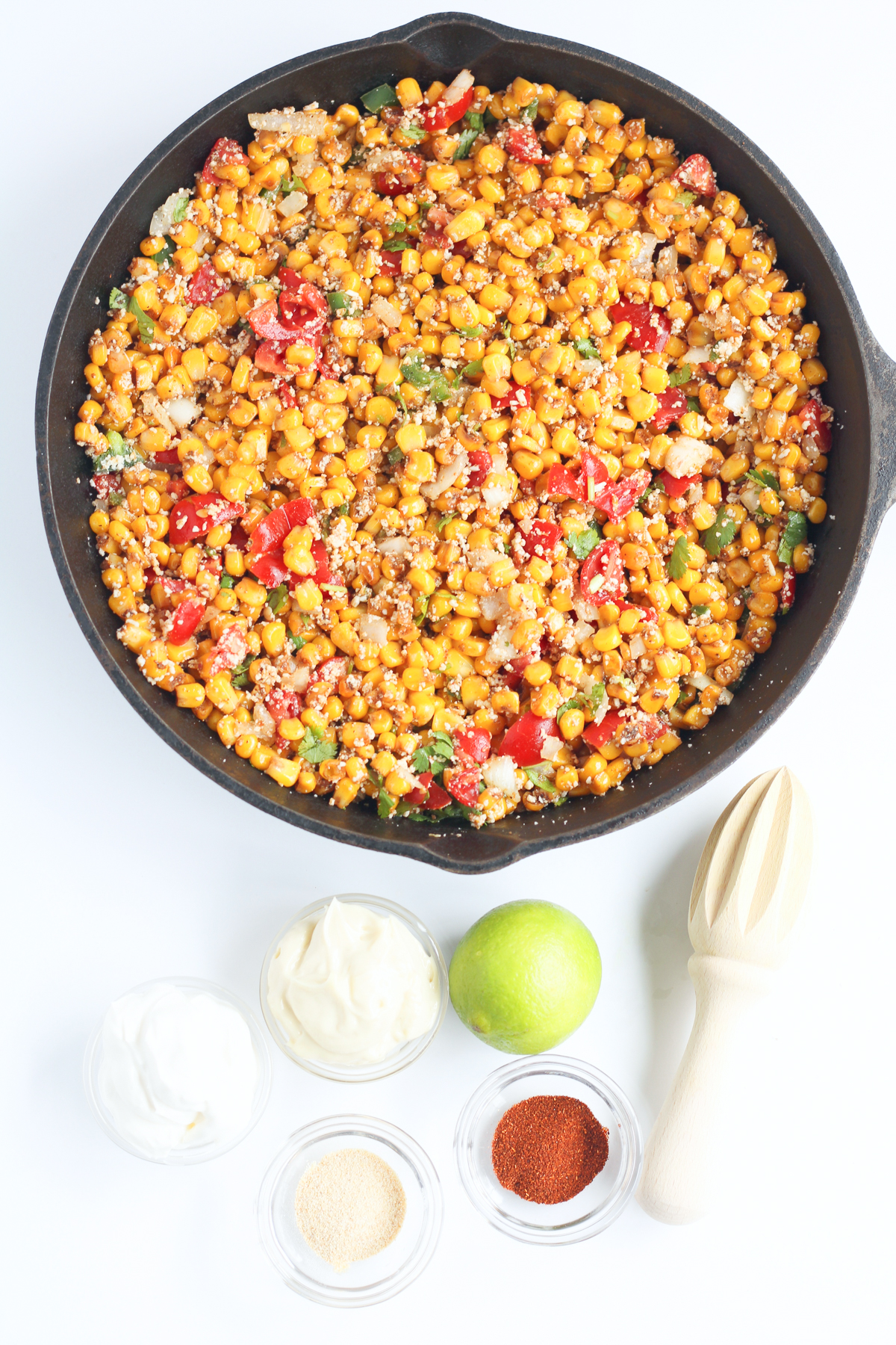 Corn with tomatoes and other vegetables in a skillet with ingredients for the sauce nearby on the table from overhead.