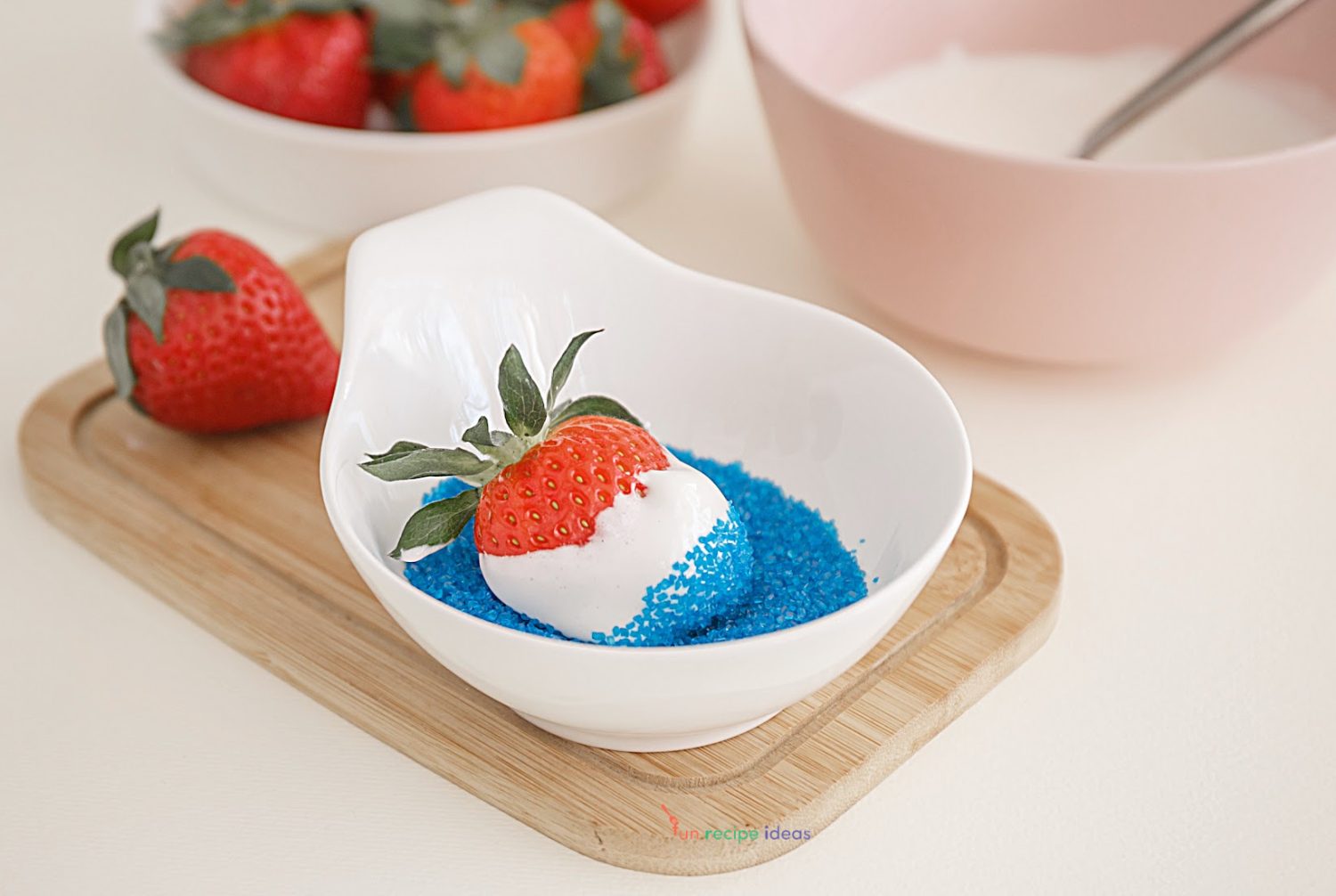 marshmallow dipped strawberry being pressed into blue colored sugar.