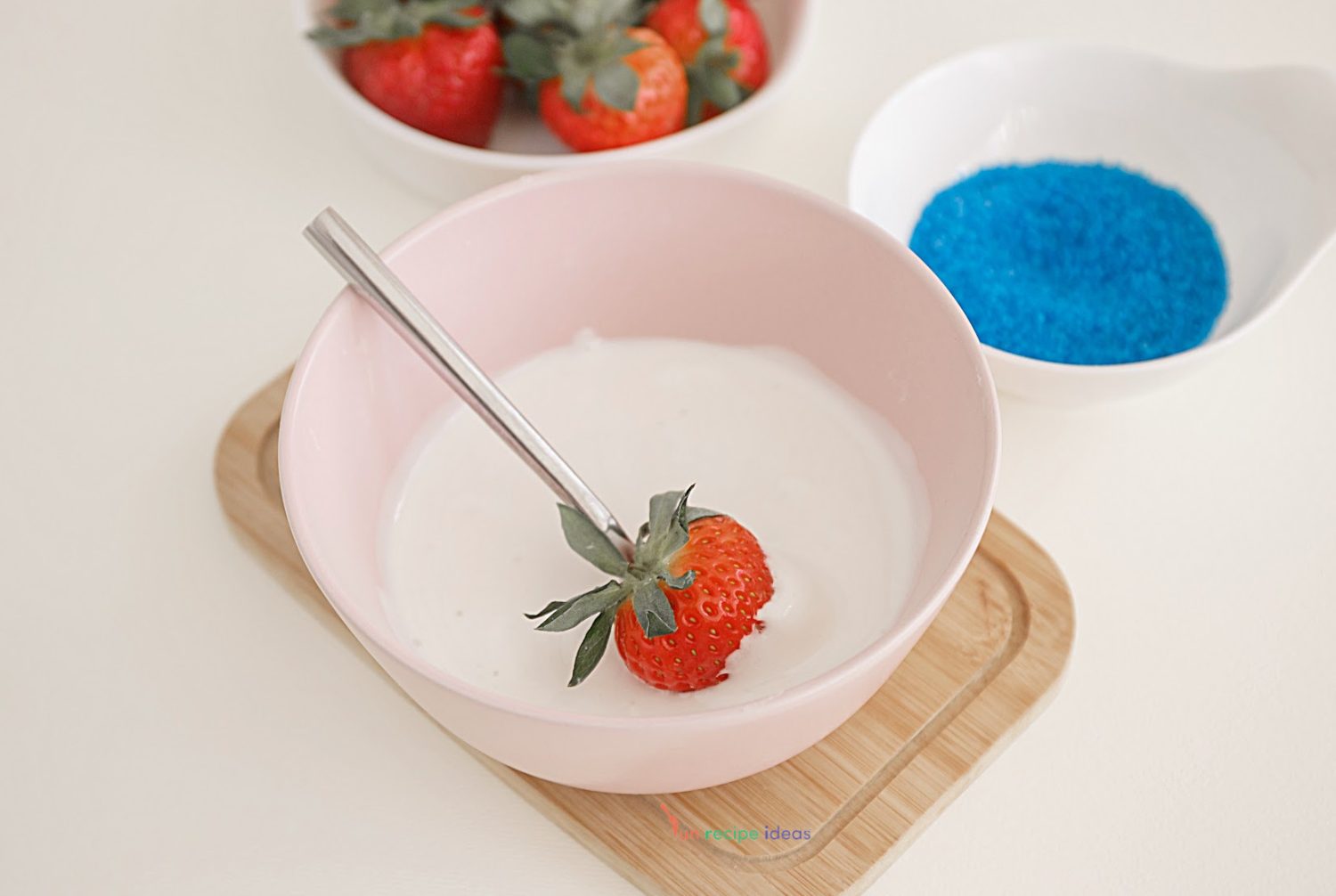 spoon dunking a strawberry into white marshmallow cream.