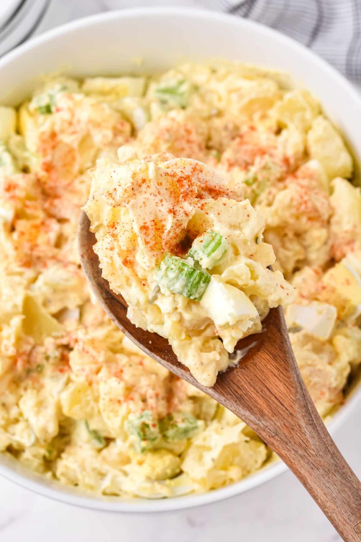 yellow potato salad with paprika and chopped celery on wooden spoon
