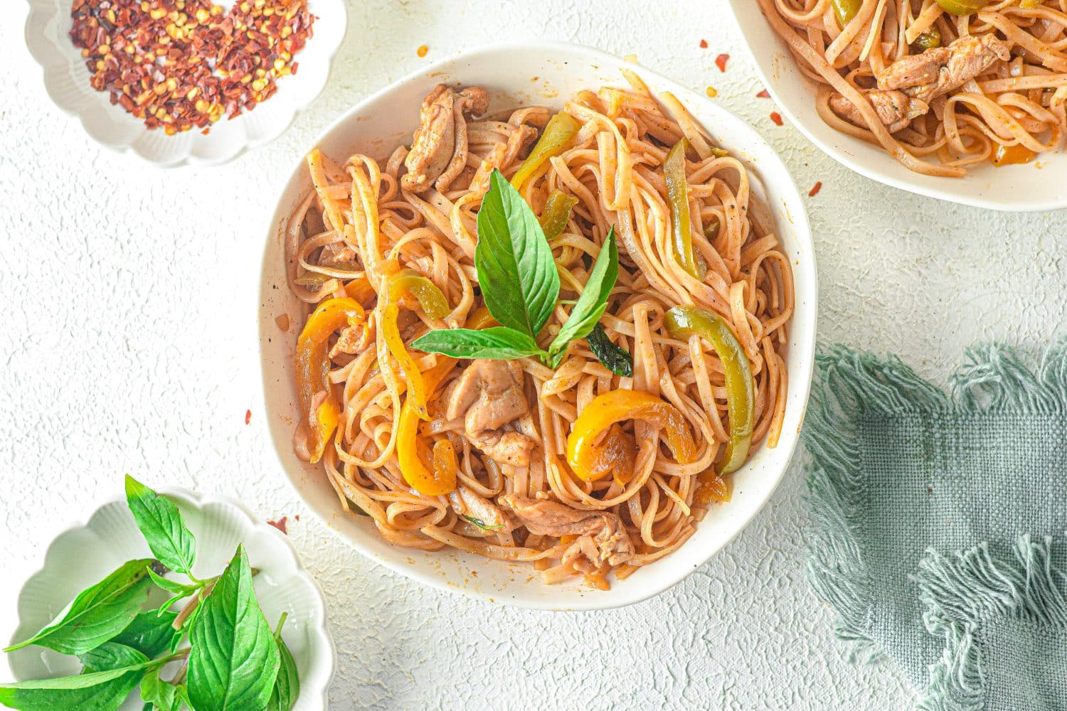 drunken noodles in white bowl with basil on top