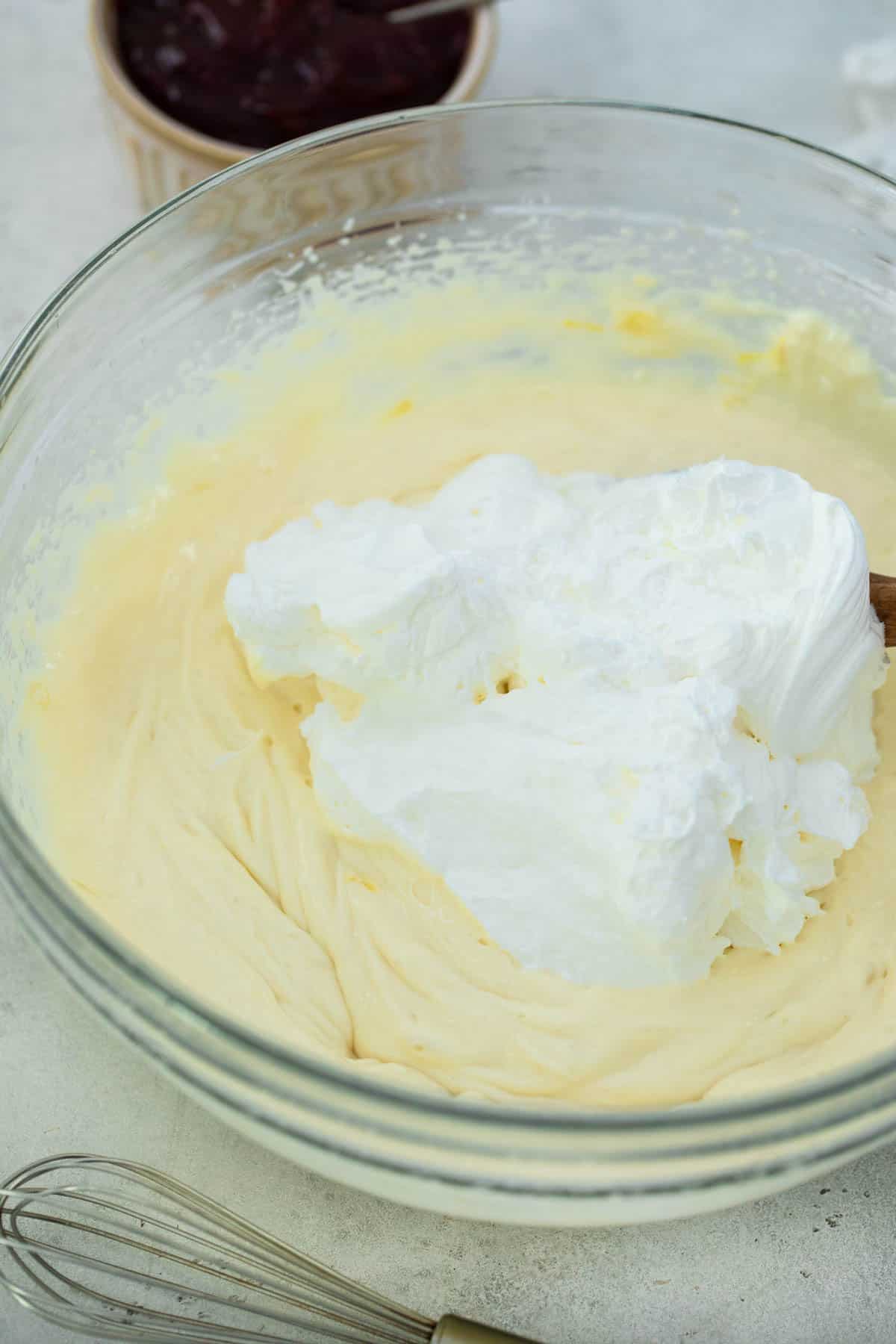 Whipped cream being added to cream cheese mixture in clear glass bowl