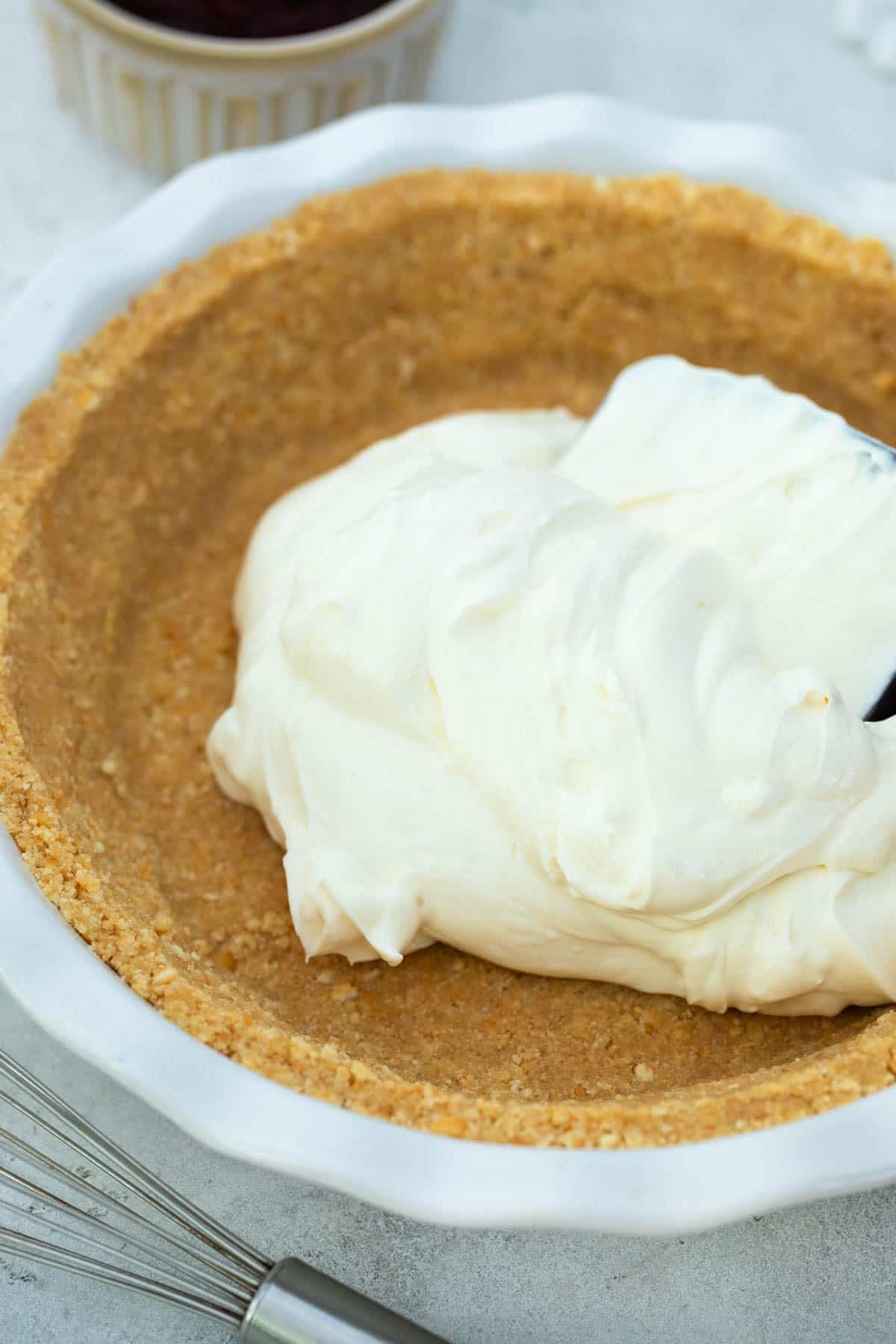 Cheesecake being added to a graham cracker crust in a white pie dish