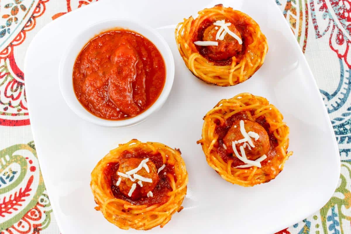 Three spaghetti muffins with a bowl of marinara on a plate.
