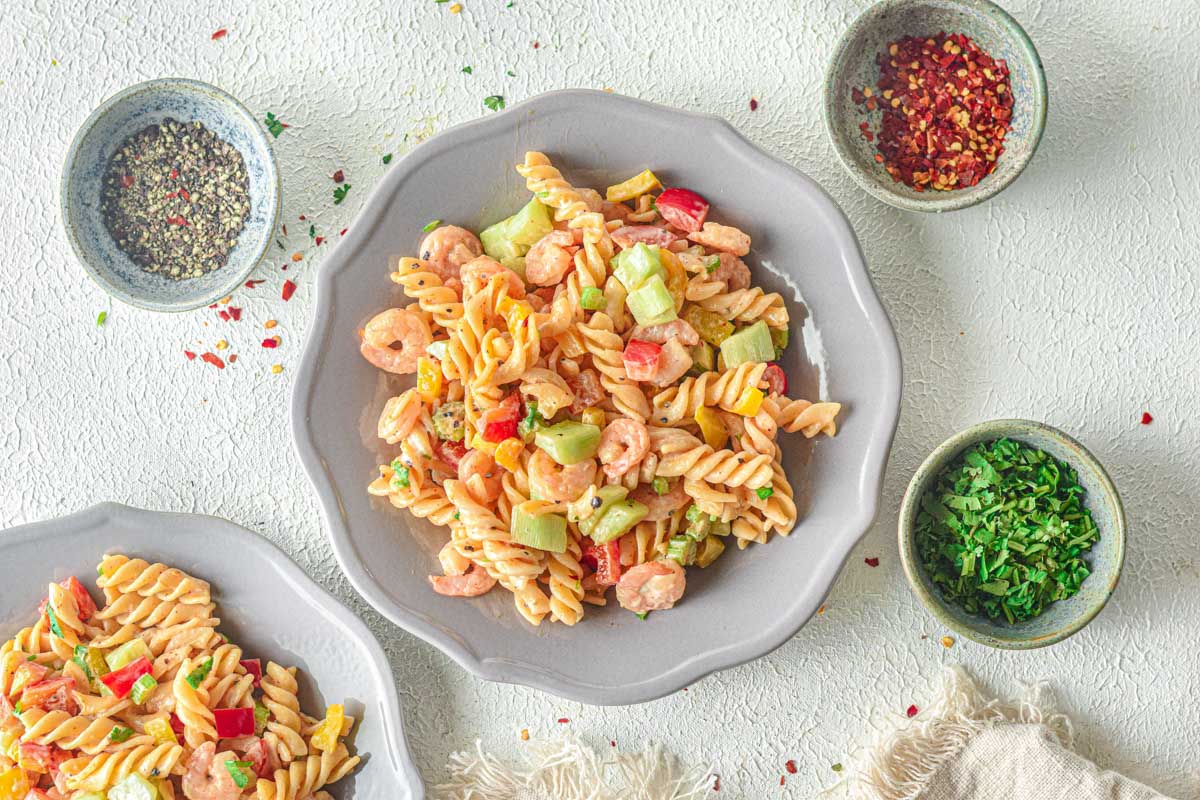 shrimp pasta in gray bowl on counter with spices on side