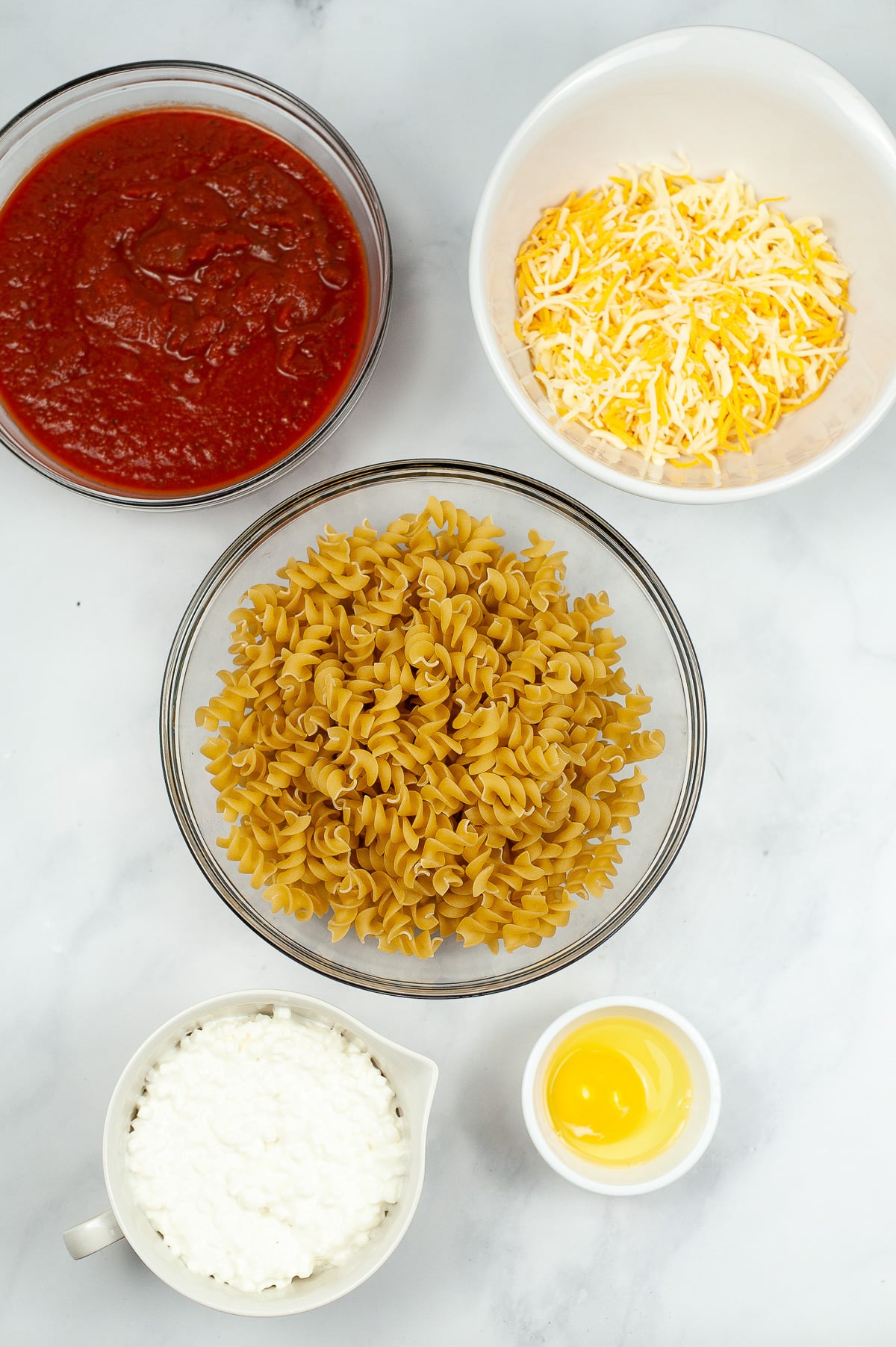 Ingredients for cheesy rotini bake in bowls from overhead.