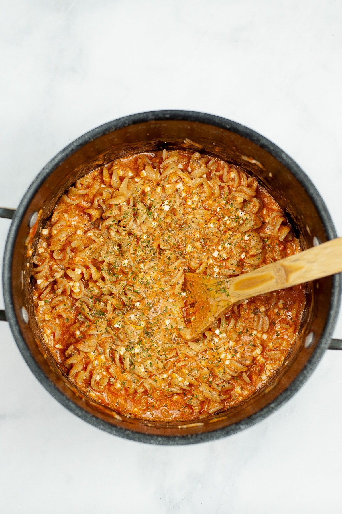 Cheesy rotini pasta cooked and mixed with pasta sauce in a large pot being stirred with a wooden spoon.