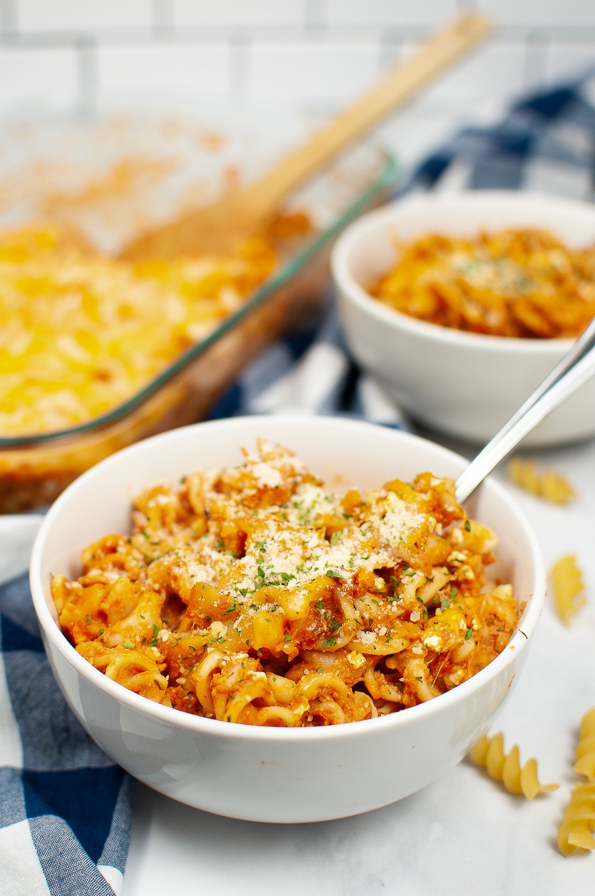 Cheesy rotini bake and sauce in a bowl with a casserole dish behind.