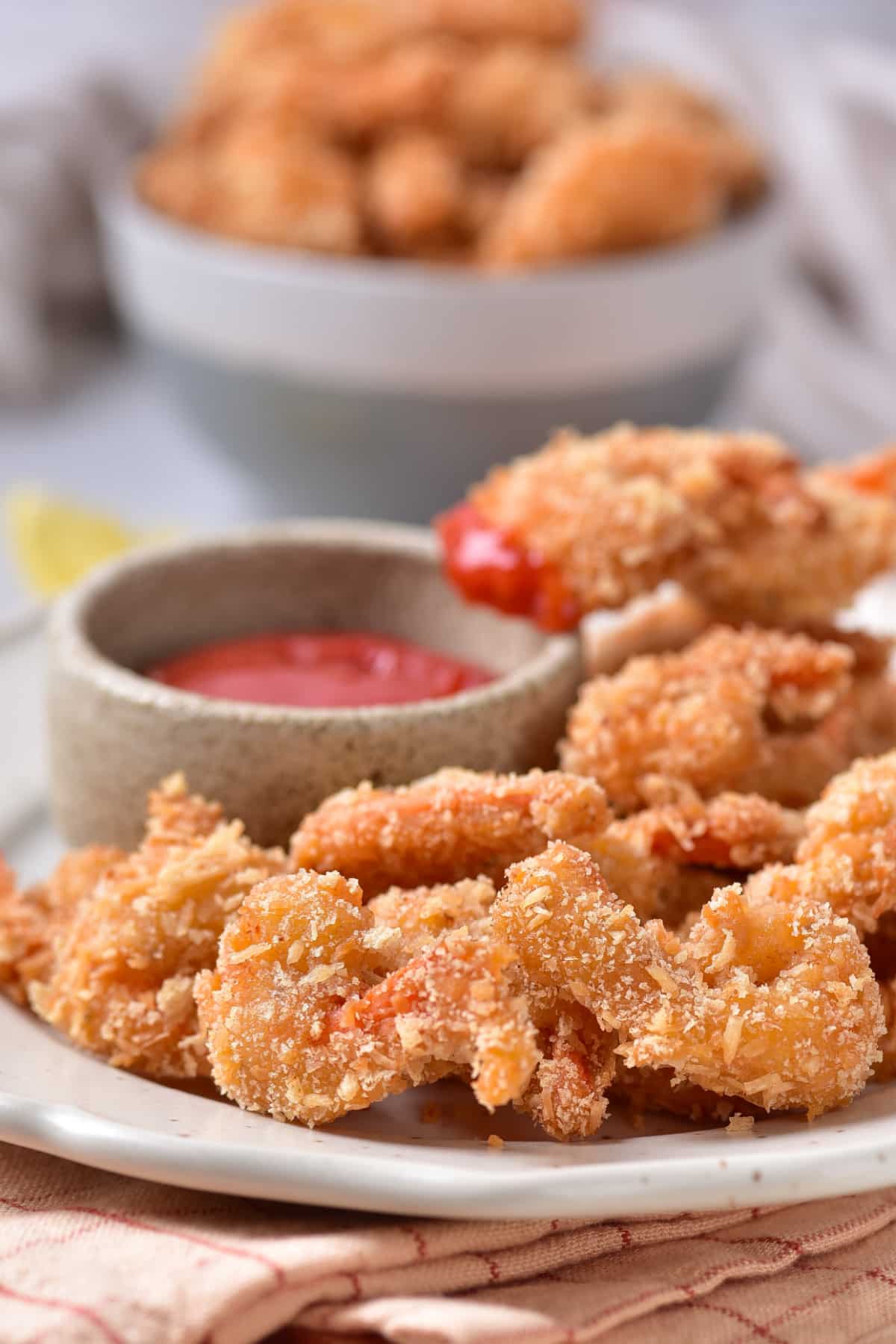 Coconut shrimp on a light colored plate with dipping sauce in the background