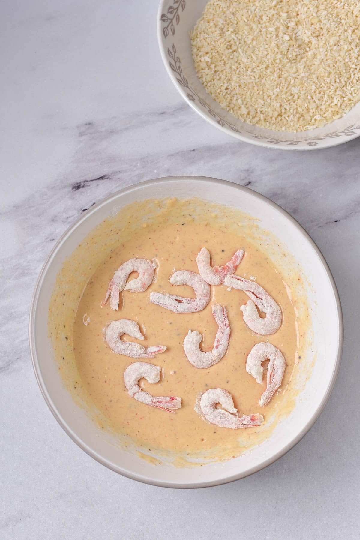 Flour covered shrimp dipped in batter in white bowl