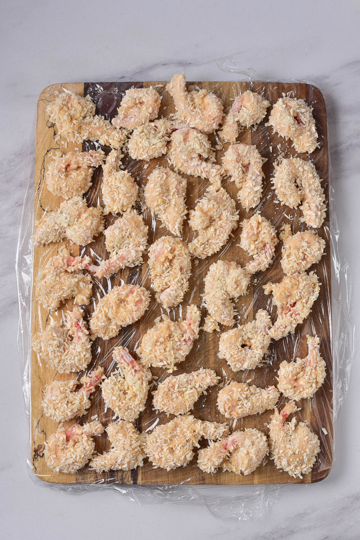 Coconut covered shrimp on a cutting board lined with plastic wrap