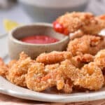 Coconut shrimp on off-white plate with dip in background