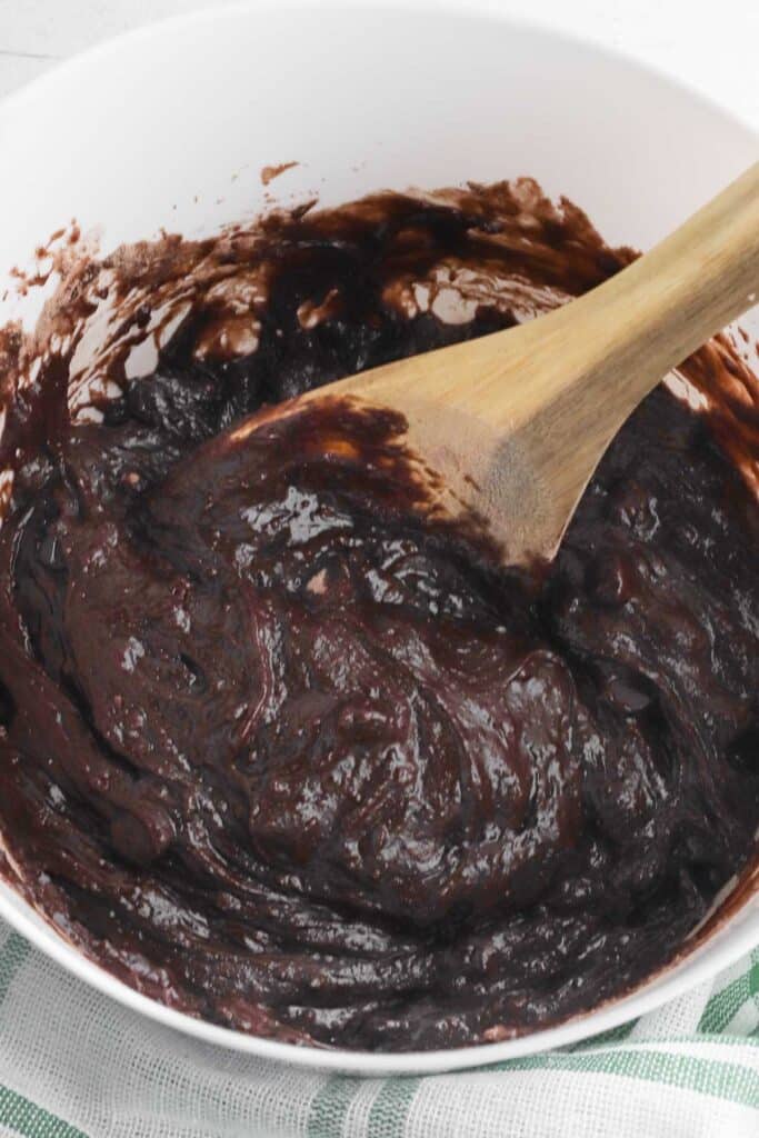 brownie batter in a white bowl being stirred with a wooden spoon.