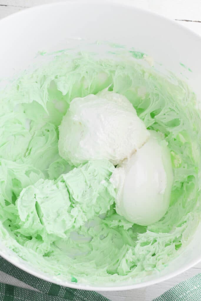marshmallow fluff in a green cream cheese mixture in a white bowl.