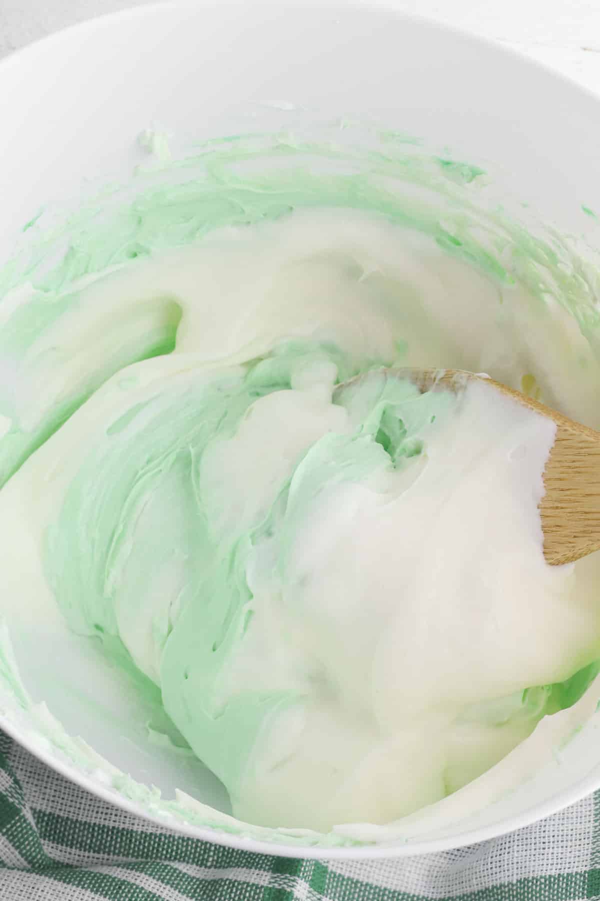 green colored cream cheese and marshmallow fluff being mixed with a wooden spoon.