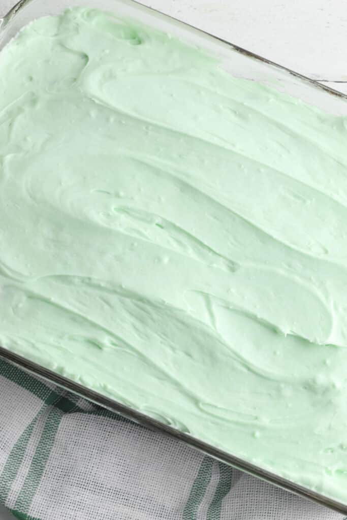 green cream cheese frosting over a brownie base in a rectangle glass dish.