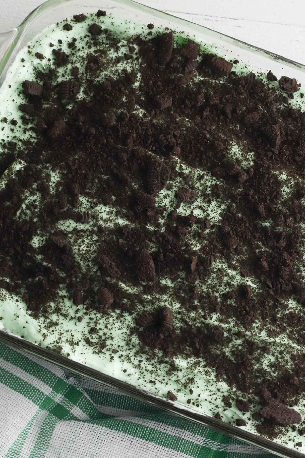 grasshopper brownie recipe with green creamy layer topped with cookie crumbs in a 9x13 glass dish.