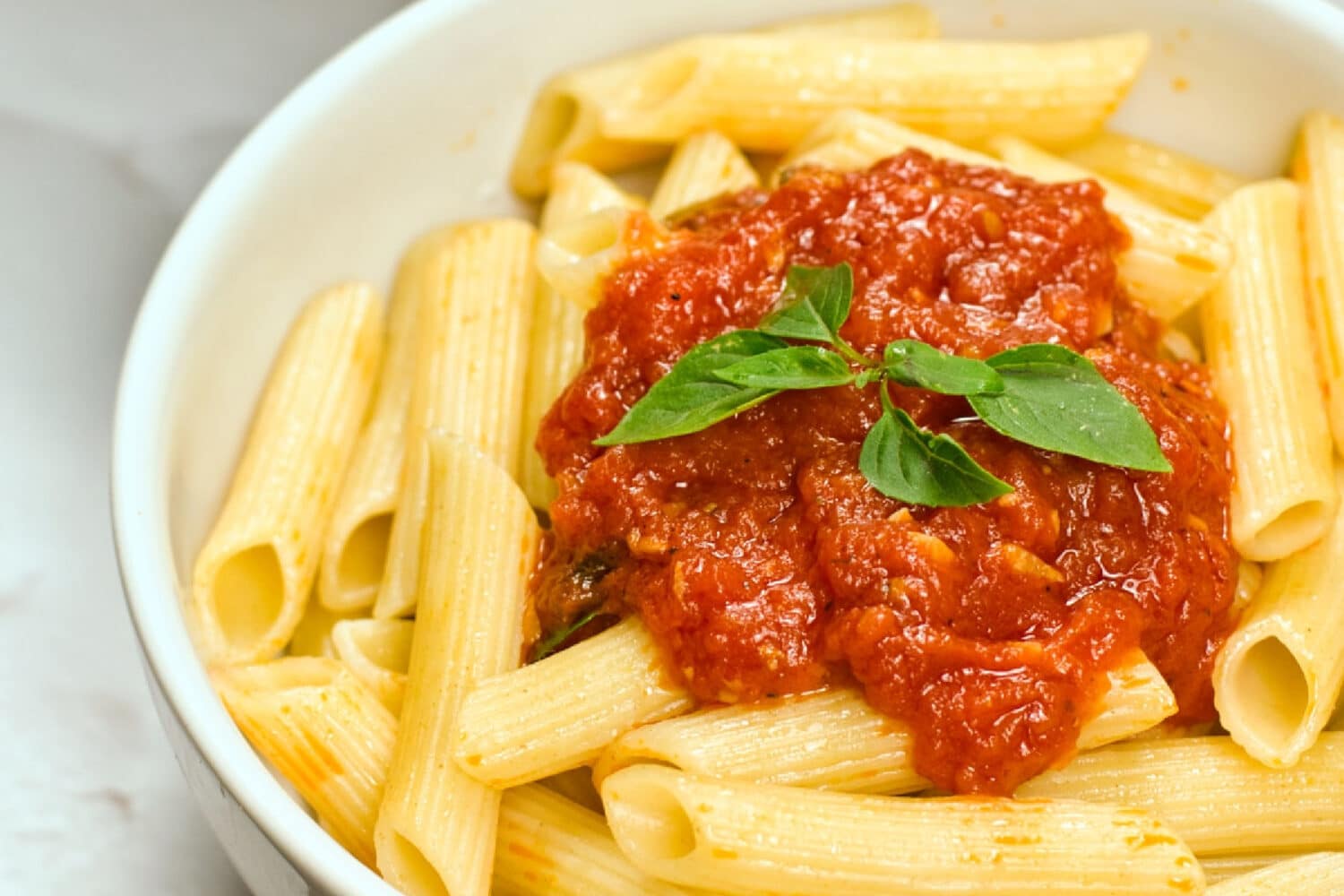 Marinara sauce on top of a bowl full of ziti with a basil leaf on top.