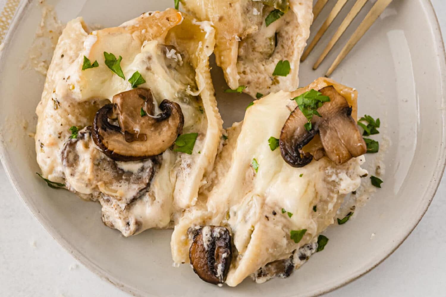 Three cheesy philly cheesestrak stuffed shells topped with mushrooms on a plate.